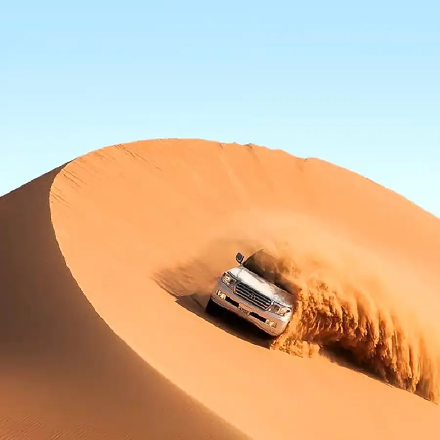 A wide-angle view of a premium Dubai desert safari camp at sunset with 4x4 vehicles on red sand dunes.